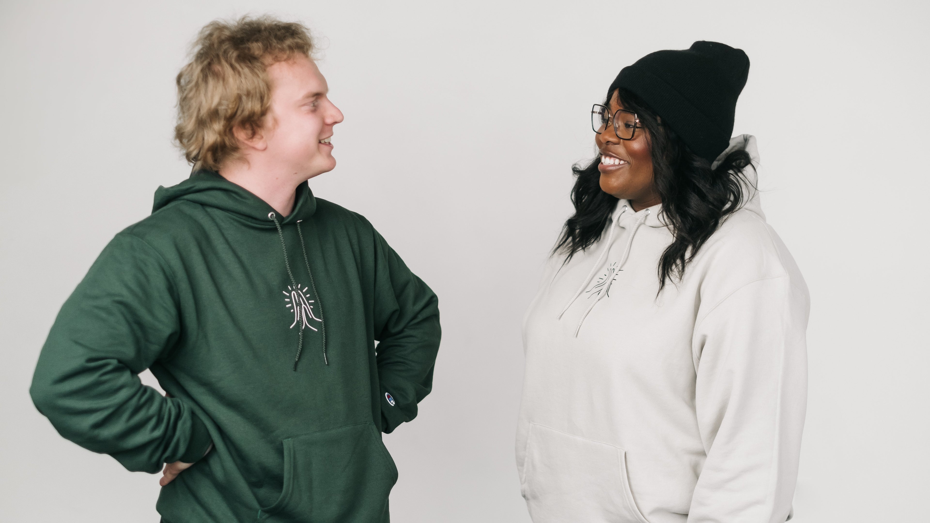 Two people wearing hoodies standing against a plain background